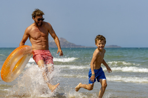 Un père et son fils jouent et courent dans les vagues à Camping Saint Pabu Plage - Glamping Bretagne.