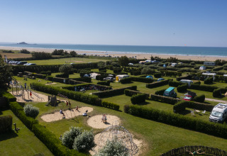 Strandcamping met hagen, kampeerplaatsen, tenten, campers en speeltuin, panorama van bovenaf.