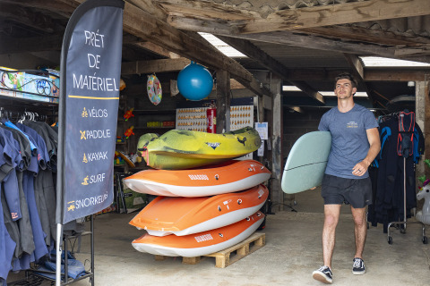 Man with surfboard at equipment rental in Camping Saint Pabu Plage - Glamping Bretagne, France.