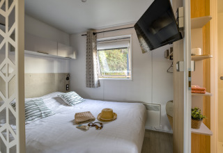 Lichte glampingkamer bij Camping Saint Pabu Plage met tweepersoonsbed, tv aan de muur en raamzicht.