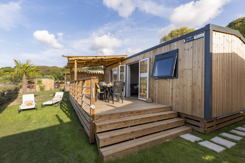 Hébergement glamping moderne avec terrasse en bois et chaises longues au Camping Saint Pabu Plage en Bretagne.