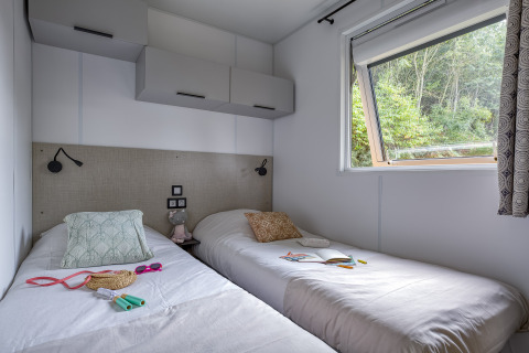 Chambre avec deux lits simples, rangements modernes et grande fenêtre au Camping Saint Pabu Plage Glamping.