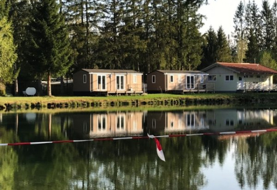 Glamping-Unterkünfte am See bei Camping Ammertal - Stacaravans Beieren, umgeben von Bäumen und Wald.