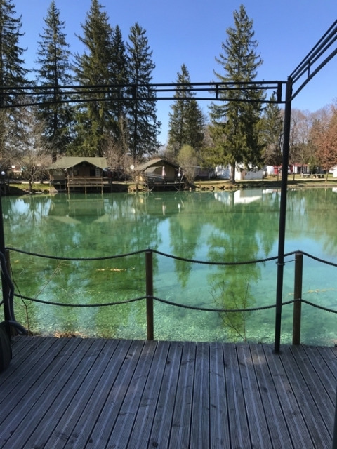 Blick auf einen klaren Teich und Glamping-Hütten bei Camping Ammertal - Stacaravans Beieren im Wald.