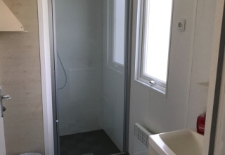 Bagno moderno con box doccia, lavabo, finestra e tappeto colorato in alloggio glamping.