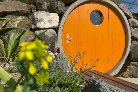 Rund, orange dør til glamping indkvartering hos Camping & Vakantiepark Orsingen i Baden-Württemberg omgivet af sten.