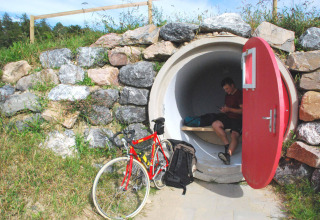 Cycliste se détend dans un hébergement glamping tubulaire à porte rouge au Camping & Vakantiepark Orsingen.