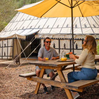 Two people enjoy breakfast at a picnic table under a parasol in front of a glamping tent at Refugio Marnes.