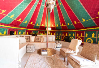 Interno colorato di tenda glamping a Refugio Marnes, Spagna, con comodi divani e arredamento orientale.