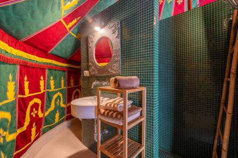 Buntes Bad mit grünen Fliesen, Holzhylde und farbenfrohem Zeltdekor bei Refugio Marnes Glamping Spanien.