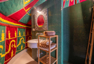 Baño colorido con azulejos verdes, estantería de madera y decoración de tienda en Refugio Marnes glamping.