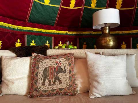 Cozy glamping tent interior with colorful fabric, patterned pillows, brass lamp, and a bowl of green apples.