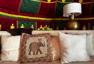 Intérieur de tente glamping avec coussins décoratifs, lampe en laiton et coupe de pommes vertes sur la table.