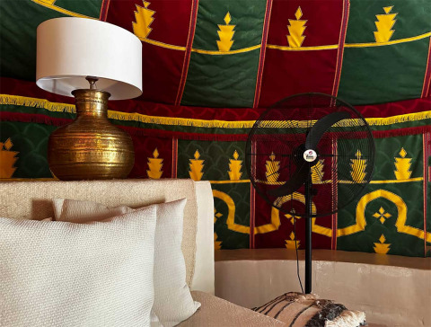 Interior view of a luxury glamping tent at Refugio Marnes with brass lamp, fan, and colorful fabric panels.