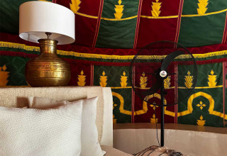 Interno di una tenda glamping di lusso al Refugio Marnes con lampada in ottone, ventilatore e tessuti colorati.