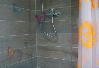 Douche met vlinderdecoratie en oranje gordijn in een glamping lodge van Camping Altschmiede, Rijnland-Palts.