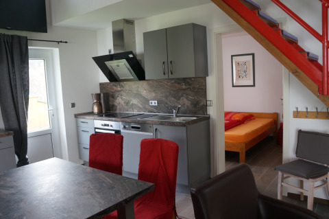 Cuisine moderne avec chaises rouges, escalier et chambre en arrière-plan dans un lodge de glamping.