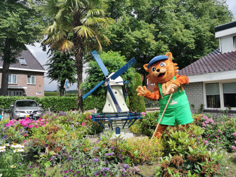 Mascotte di gatto vicino a un mulino a vento in miniatura nei giardini di Vakantiepark De Oude Molen - Safaritent Gelderland.