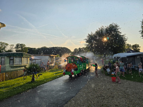 Kinderen spelen met waterpistolen bij safaritenten op Vakantiepark De Oude Molen, terwijl een treintje langskomt.