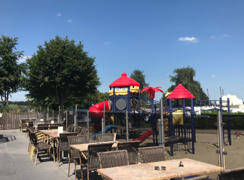 Espace de restauration extérieur avec tables et chaises près d'une aire de jeux à Vakantiepark De Oude Molen - Safaritent Gelderland.
