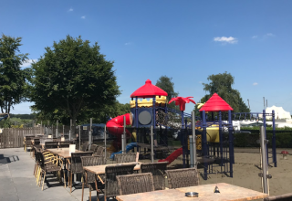 Outdoor dining area with tables and chairs next to a playground at Vakantiepark De Oude Molen - Safaritent Gelderland.