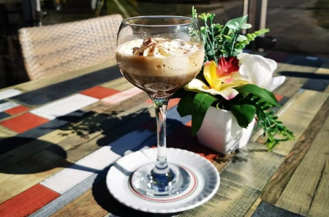 Een glas dessertkoffie met slagroom op een kleurrijke houten tafel bij Vakantiepark De Oude Molen - Safaritent Gelderland.