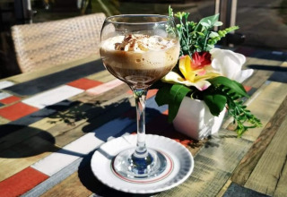 Een glas dessertkoffie met slagroom op een kleurrijke houten tafel bij Vakantiepark De Oude Molen - Safaritent Gelderland.