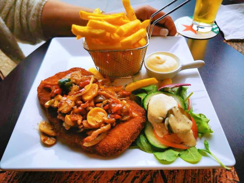 Une assiette de frites, viande panée avec sauce aux champignons, salade fraîche et sauce servies à table.