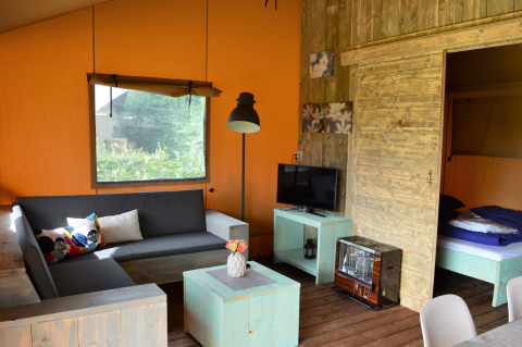 Glampinginterieur met zitbank, tv, houten meubels en slaapkamer in een safaritent in Gelderland.