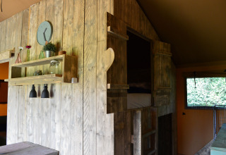 Intérieur douillet d'une cabane glamping au Safaritent Gelderland avec murs en bois et étagères décoratives.