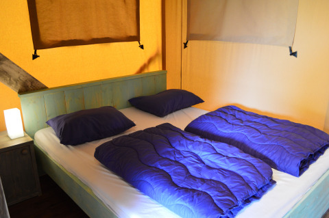 Gemütliche Glamping-Unterkunft mit Doppelbett und blauer Bettwäsche in Safaritent Gelderland, Niederlande.