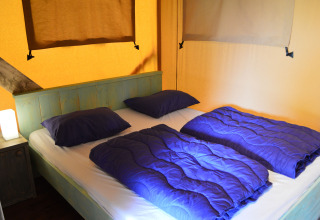 Comfortabele glampingaccommodatie met een tweepersoonsbed en blauw beddengoed in Safaritent Gelderland.