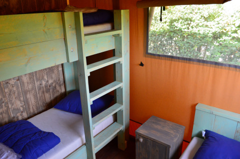 Interior de alojamiento glamping con literas, cojines azules y ventana con vistas en Safaritent Gelderland.