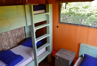 Innenraum einer Glamping-Unterkunft mit Etagenbett, blauen Kissen und Fenster bei Safaritent Gelderland.