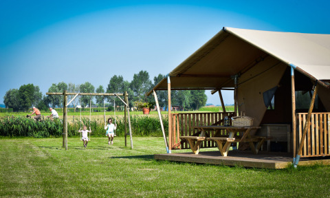 Glamping - aan de Vleterbeke : Enfants sur des balançoires près d'une tente glamping dans un champ verdoyant.