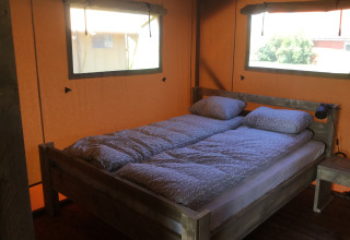 Bedroom with wooden frame bed and natural light in glamping accommodation at Glamping - aan de Vleterbeke.