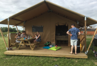 Gezin geniet van een maaltijd op de veranda van een glampingtent bij Glamping - aan de Vleterbeke.