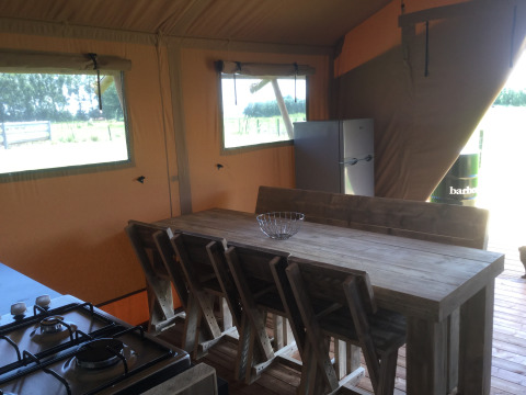 Interieur van Glamping - aan de Vleterbeke met houten tafel, stoelen, koelkast en gasfornuis in een tent.