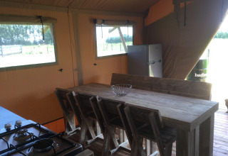 Interior of Glamping - aan de Vleterbeke featuring a wooden table, chairs, fridge, and gas stove in a tent.