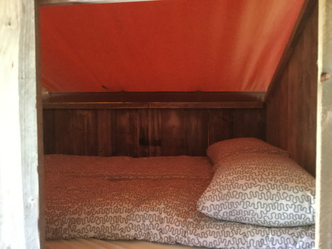 Zona para dormir en Glamping - aan de Vleterbeke con interior de madera y techo de tienda naranja.