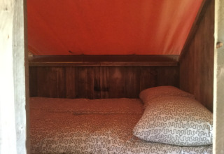 Coin couchage à Glamping - aan de Vleterbeke, intérieur en bois et toit de tente orange chaleureuse.