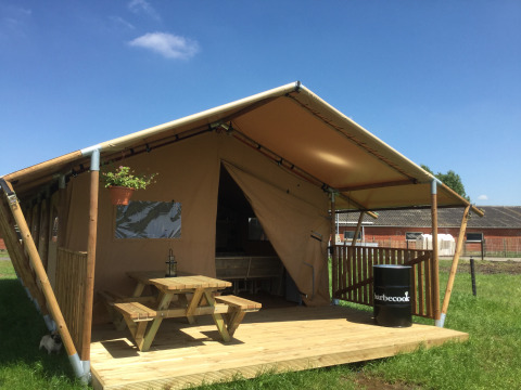 Glamping ‘Glamping - aan de Vleterbeke’ met houten terras, picknicktafel en barbecue nabij de tent op een veld.