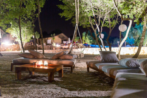 Outdoor lounge area at night in Camping Nono Ban - Safaritenten Brac with sofas, cushions, and candlelight.