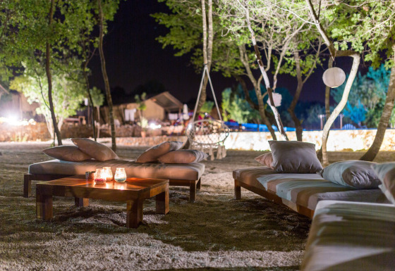 Area lounge all'aperto di notte al Camping Nono Ban - Safaritenten Brac con divani e candele accese.