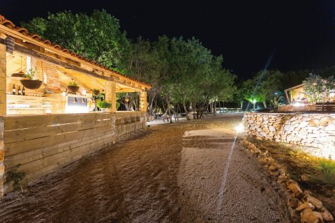 Avondbeeld van Camping Nono Ban - Safaritenten Brac met gezellige verlichting, veel groen en houten verblijven.