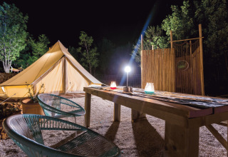 Glamping at Camping Nono Ban - Safaritenten Brac with a tent, deck chairs and table lit up at night.