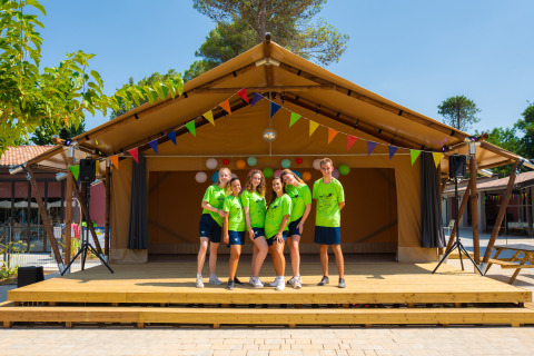 Cinco jóvenes con camisetas verdes posan sonrientes en el escenario exterior de Trasimeno Glamping Resort con banderines.