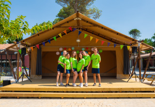Vijf jongeren in groene shirts poseren op het podium bij Trasimeno Glamping Resort met kleurrijke vlaggetjes erboven.