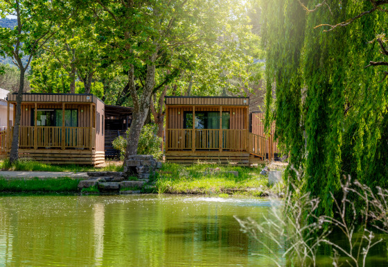 Deux cabanes en bois près de l’eau au Trasimeno Glamping Resort - Cottages Umbrië, entourées d’arbres verdoyants.