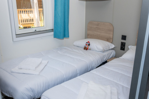 Dos camas individuales blancas en una habitación luminosa con ventana y cortina azul en Trasimeno Glamping Resort.